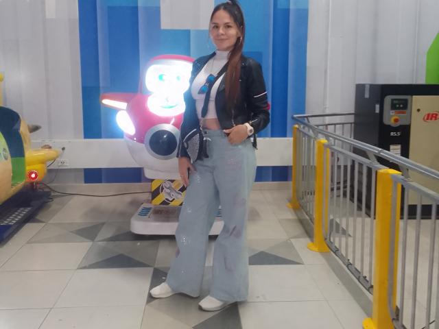 IvoryFlame with long brown hair, wearing a black jacket, white top, blue tie, and high-waisted, flared, light blue pants, standing in front of a robot toy.