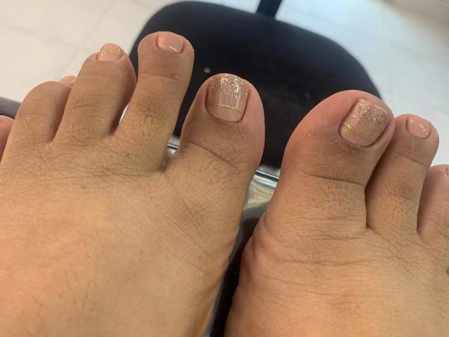 Salmahad's feet with her toes showing off a glossy, gold glitter nail polish on the tips, her skin is light brown and the nails are neatly trimmed.