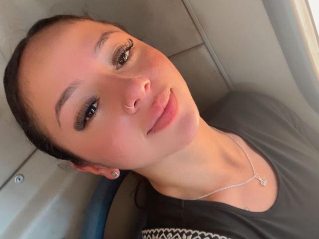 KloeThompson has a nose ring, subtle makeup, and a gentle smile, wearing a black shirt with a small white pattern. She's lying down, looking relaxed.