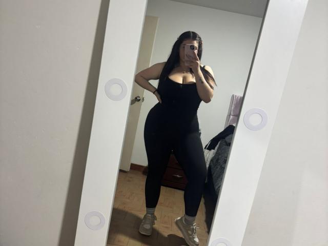 VenusxMusa in a black tank top and tight black leggings, showing off her curvy ass and large tits, taking a mirror selfie with one hand on her hip.