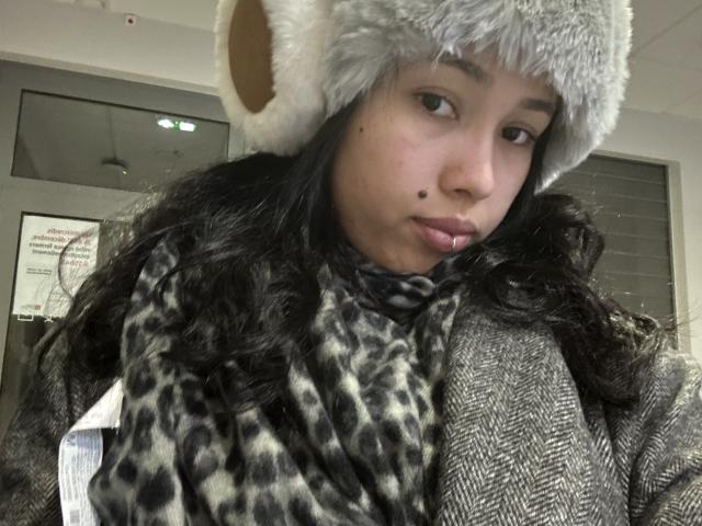 NashiroSakuraii with a cute gray furry hat, leopard print scarf, and houndstooth coat, pouting slightly, showing a small beauty mark on her left cheek.