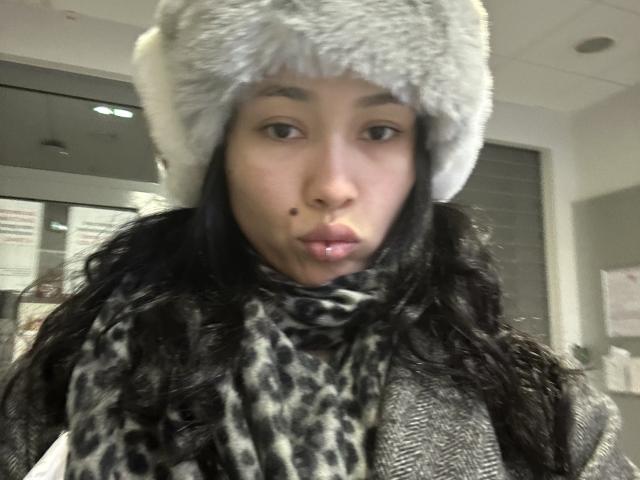NashiroSakuraii with a grey fur hat, leopard print scarf, and wintery grey coat, puckering her lips in a slightly pouty expression. She has a small beauty mark on her left cheek.