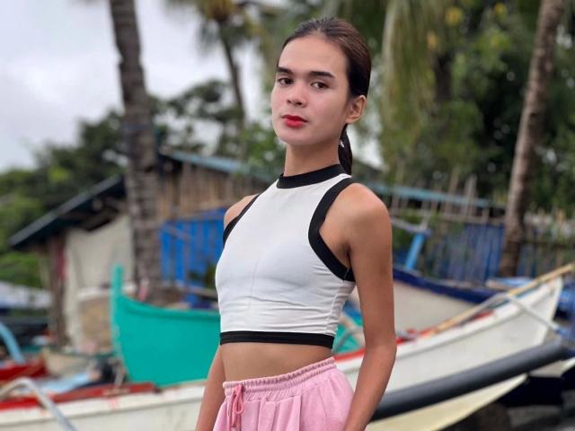 PeachAnderson-hot has small tits, a slim waist, and pink pants, wearing a white and black sports top, standing by boats with a tropical background.