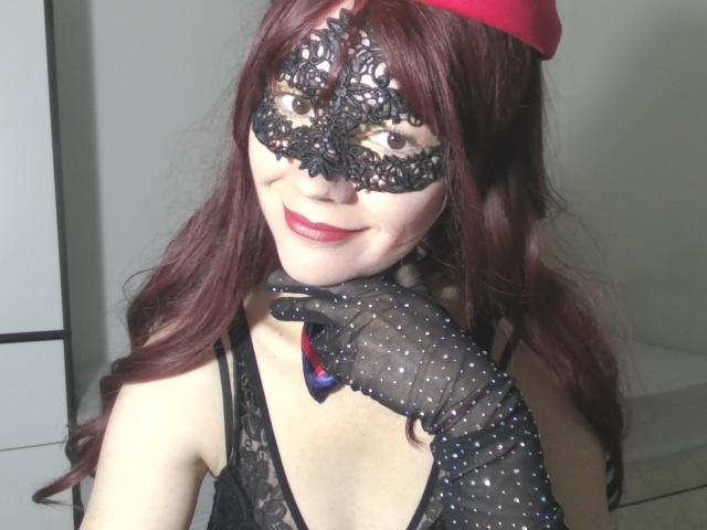 AromaLove with red hair, black lace mask, and sheer polka-dot gloves, smiling with red lipstick, wearing black lace lingerie, red hat, and a blue ribbon on the glove.
