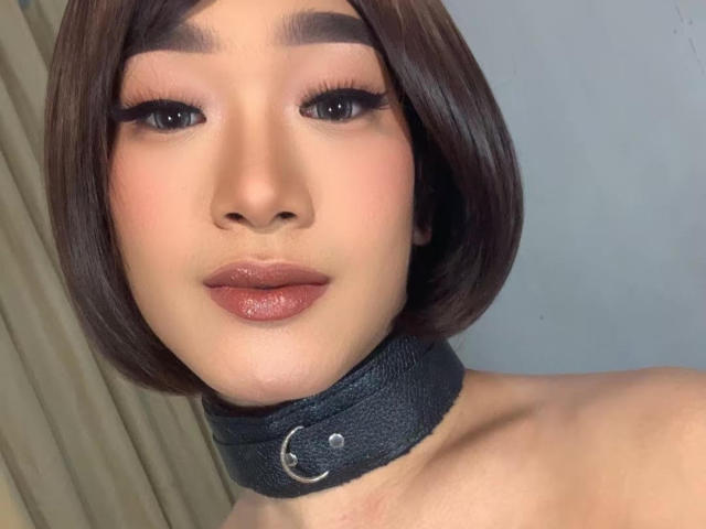 AsianHugeCockxX with a shiny brown bob, thick eyebrows, long eyelashes, glossy pink lips, wearing a black leather choker with a silver ring, no top visible.
