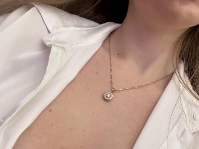 NancyChaude's white shirt, slightly open, showing her neck and chest with a gold necklace featuring a small, round, diamond-encrusted pendant. Her skin is fair with some freckles.