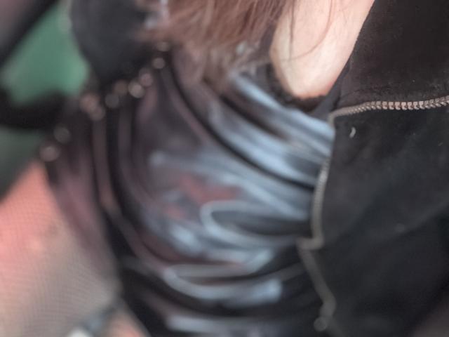 LaurentColin's chest in a tight, black leather shirt with visible zippers, showing a slight peek of their tits. Brown hair falls over their shoulder. Blurred, close-up shot.