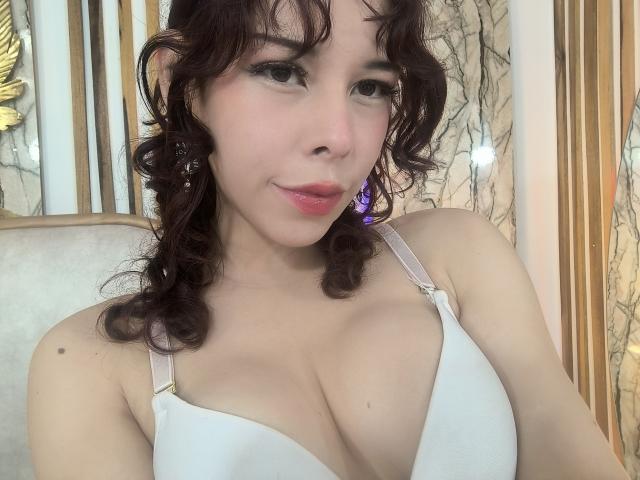 Savanah Reed tiene el pelo castaño rizado, piel clara y lleva un sujetador blanco que deja ver sus grandes senos. Está sonriendo, con lápiz labial rosa y pendientes morados..