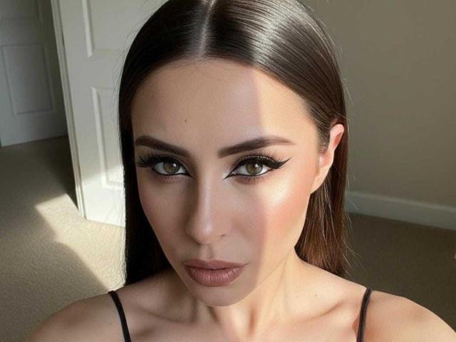 KimyR has dark brown, straight hair, green eyes with thick black eyeliner, and full pinkish-brown lips. She's wearing a black spaghetti strap top, looking directly at the camera.