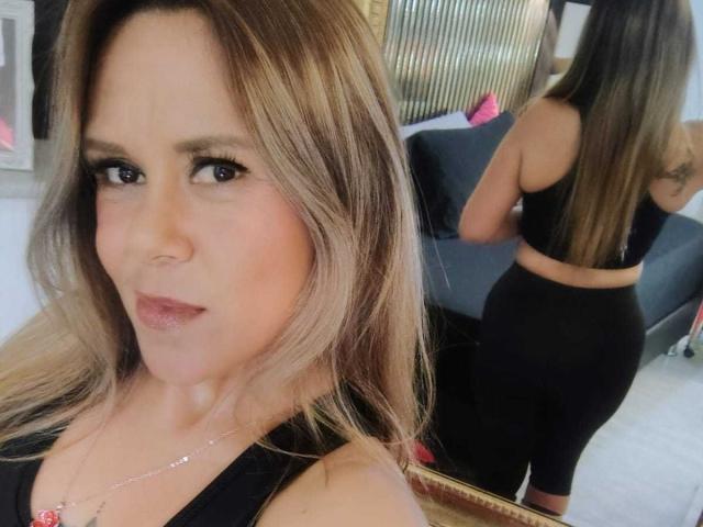LilithBonneth has blonde hair, black eyeliner, and is wearing a black top and black pants, showing her ass in a mirror reflection, with a subtle smile.
