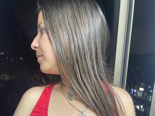 GraceRedMiller with long, straight brown hair, red top, and silver necklace, looking to the side, showing her profile and smooth, fair-skinned face.