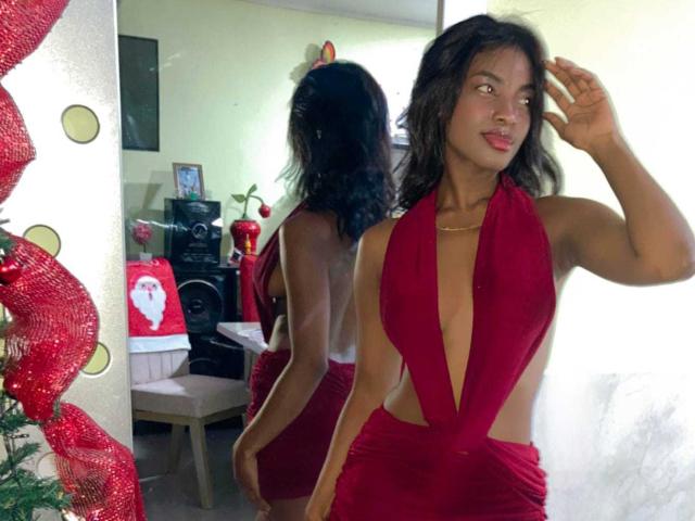 HazelClark with dark wavy hair, red halter dress showing her tits and ass, standing in front of a mirror, smiling, hand on head, Christmas decorations in the background.