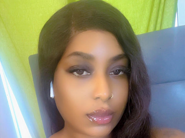 Solene69 has dark brown, straight hair, a nose ring, and shiny purple lipstick. She has black eyeliner and medium brown skin. She's wearing white earbuds.