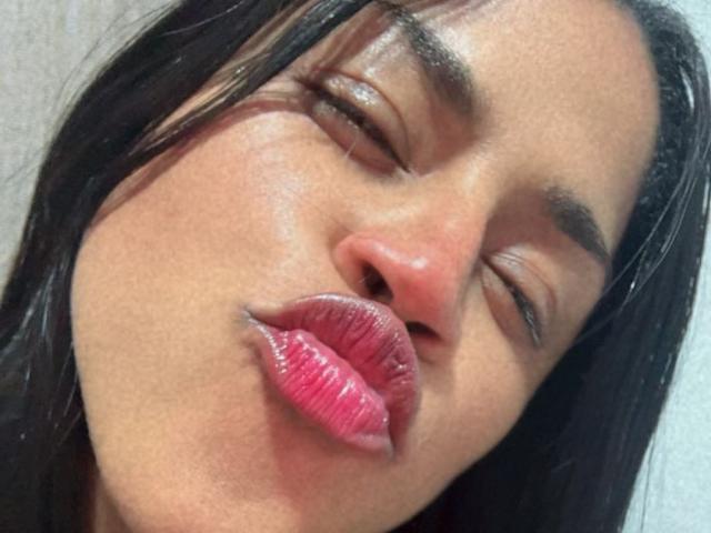 IvannaDuran's face, eyes closed, puffy pink lips slightly parted, dark straight hair, tan skin, subtle sheen, and full eyebrows. Her expression is soft and relaxed.