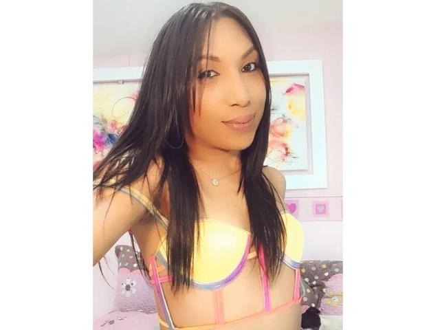 VellenBiggAss has long black hair, small yellow and pink bikini top, and a cute smile. She's showing off her tits in a selfie, with a subtle, confident look.