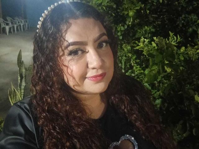 SeleneFhox69 has curly brown hair, a pearl headband, and is wearing a black top with a silver design. Her pink lips and dark eyebrows are visible.