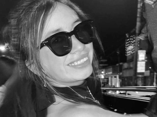 Black and white selfie of AnyuWu with large tits, smiling, wearing dark sunglasses, and a necklace, her long hair loose, in a city night setting.