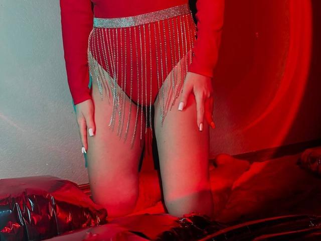 BalletSwan in red long-sleeve top and silver chain fringe over red panties, kneeling on red leather, hands on thighs, red and pink lighting, visible white nails.