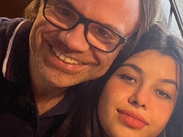 Viktor has a beard, glasses, and a happy smile, next to Penny with pouty lips. Both are smiling at the camera, with Viktor's arm around Penny's shoulder.