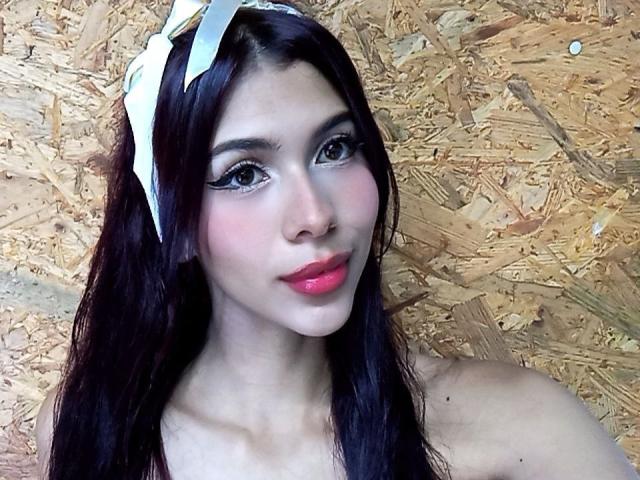 DanikaSerov with long black hair, white headband, pink lipstick, and thick eyeliner, showing off her cute face and bare shoulders. Her tits are not visible.
