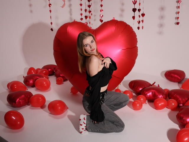 MargaritaKis with red heart balloons, kneeling, wearing black top, gray pants, white socks with red hearts, looking at camera, hands covering small tits. Red and red balloons scattered.