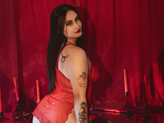 ScarletPriynce with long black hair, red lingerie, tattoos on arm and shoulder, looking back, red candles, red curtain, seductive, red lips, red background, sexy, curvy.