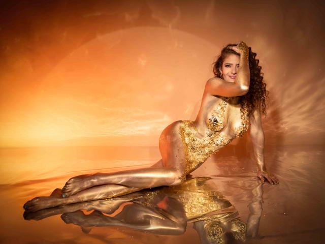 CelineBoyer with curly brown hair, lying on reflective surface, wearing gold-leafed bodysuit, covering her tits with one hand, smiling, legs stretched, reflecting in water.