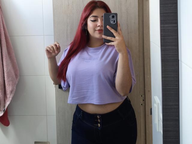 RousseColliinss with red hair, wearing a lilac crop top and black jeans, holding a phone in a mirror selfie, showing her tits and a bit of her ass.