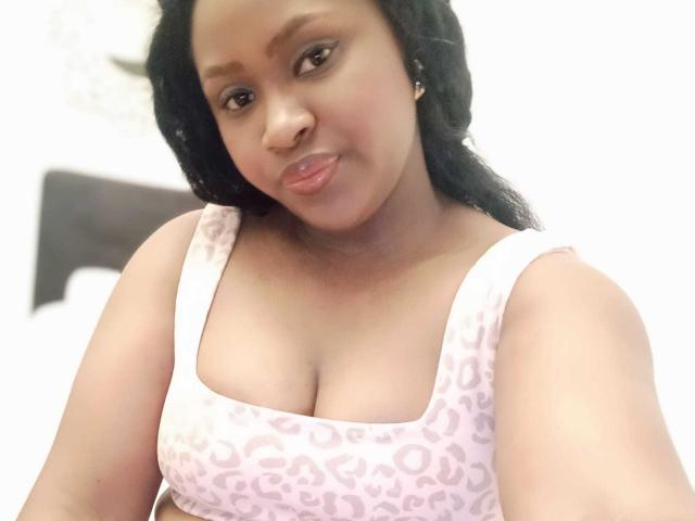 KamalaDavis has medium brown skin, black wavy hair, and is wearing a pink leopard-print tank top showing her boobs. She's smiling slightly with a soft, cute look.