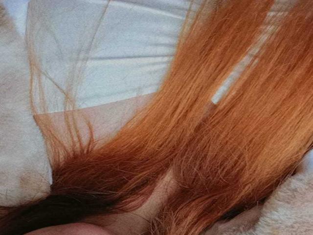 AmberLaurent's orange hair is in the foreground, covering her white top and a small part of her bare, pale skin. The image focuses on her long, straight hair.