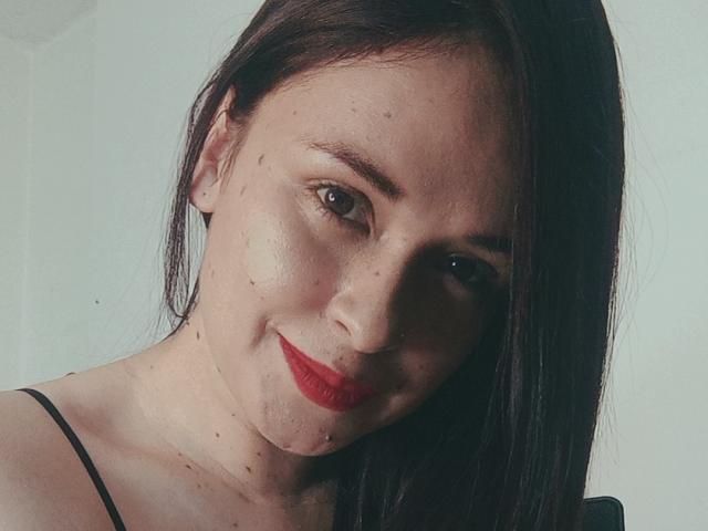 WendySchulz has red lipstick, dark straight hair, and a slight smile. Her freckled face is close-up with visible pores and a cute, slightly chubby look.