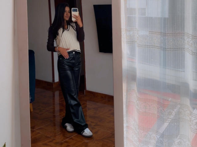 ThaliaAres with long black hair, white raglan shirt, black leather pants, and white sneakers, taking a mirror selfie, showing a slim, sexy figure with a small ass.