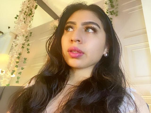 ZoeRedds has long black hair, pink lipstick, and brown eyes with long eyelashes. She's looking to the side with a slightly open mouth. Her tits are small, and she's cute.