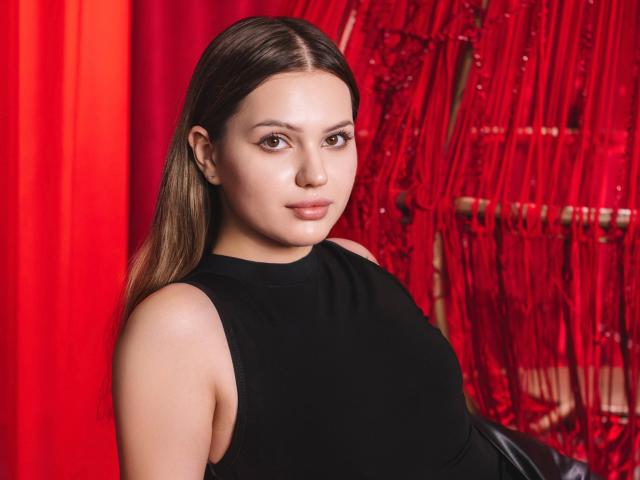 SophiaGrant has medium brown hair, a cute face, and is wearing a black sleeveless top. She has small tits and is looking at the camera with a subtle smile.
