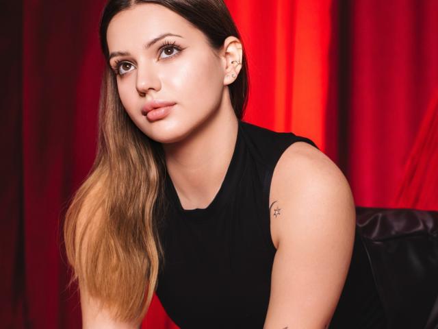SophiaGrant with light brown hair, wearing a black sleeveless top, has a small tattoo on her right arm, and is looking slightly to the left with a calm expression.