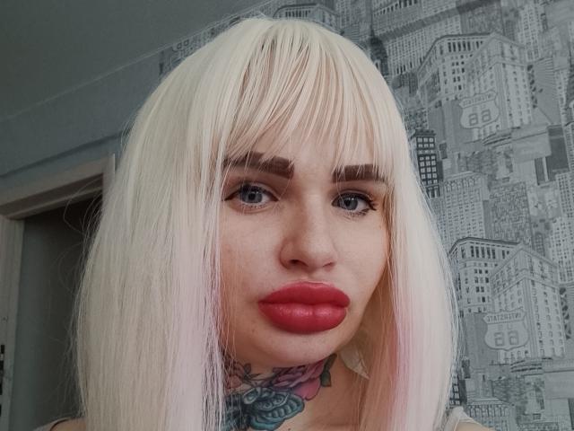 Cvetocek69 with platinum blonde hair, red lips, and a tattoo under the chin, has blue eyes, full eyebrows, and a serious expression. Boobs not visible. Ass not visible. Pussy not visible.