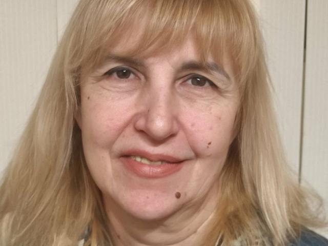 PattySanny has blonde hair, brown eyes, and a few moles on her face. She's smiling with a slight chin crease. Her nose is small and she has pink lips.