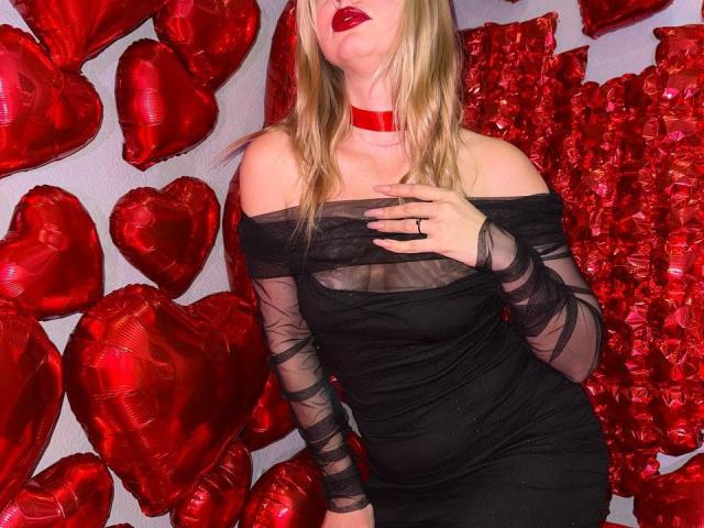 CrystalHope with blonde hair, red lips, black off-shoulder dress, sheer sleeves, red choker, hand on chest, surrounded by shiny red heart balloons, showing her ass in the dress.