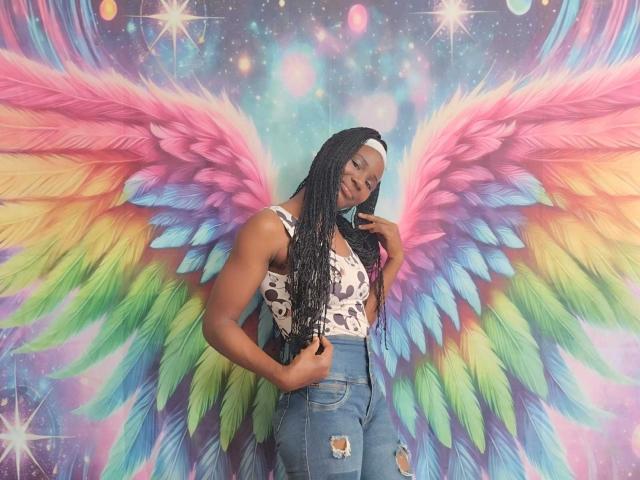 TenderBony has dark skin, long braids, wearing a white and black cow print top, and high-waisted ripped jeans. She's standing with colorful, rainbow wings behind her.