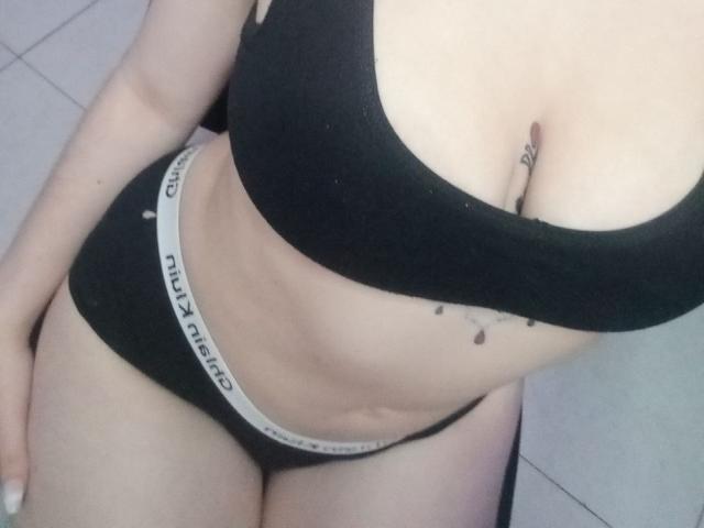 SofiaFaces tem pele clara, um sutiã preto e calcinhas pretas da Calvin Klein, mostrando seus seios e vulva, com uma pequena tatuagem abaixo dos seios. Sua mão está apoiada em sua coxa..