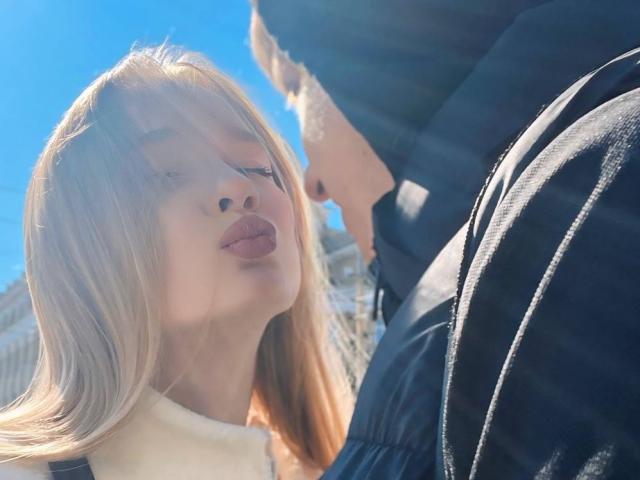 ShawtyMiaAndJack with blonde hair and pouty lips, looking up at a guy in a black puffy jacket, sunlight flaring in the blue sky. Boobs not visible.