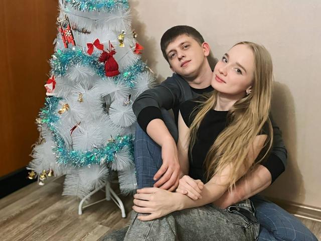 ShawtyMiaAndJack sitting on floor, ShawtyMia with long blonde hair, black top, gray pants, ShawtyJack with short brown hair, black shirt, blue jeans, white Christmas tree with blue and red ornaments.