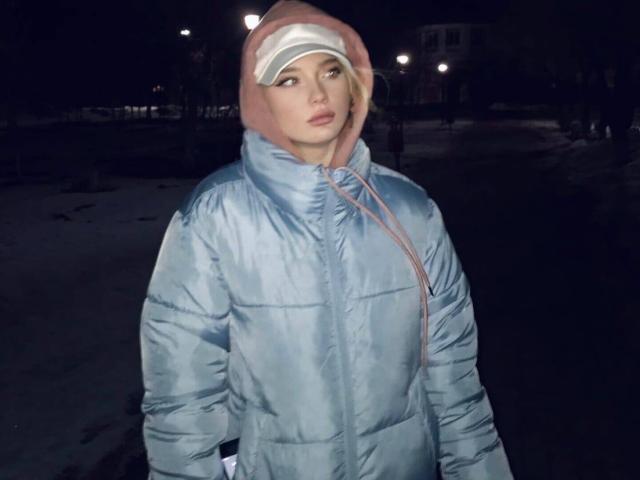 ShawtyMiaAndJack in a shiny blue puffy jacket with pink hood, white visor, and pale skin, standing in a dark, snowy night, looking off to the side.