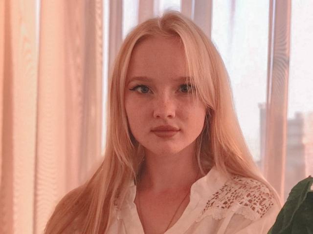 ShawtyMiaAndJack has long blonde hair, blue eyes, and freckles. She's wearing a white lace shirt with a buttoned-up collar, looking serious with a subtle pout.