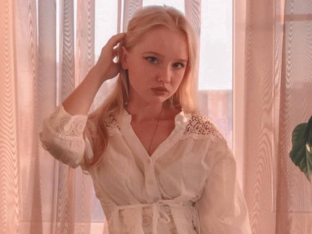 ShawtyMiaAndJack with blonde hair, wearing a white, lace-trimmed, button-up shirt, hand in hair, looking serious, soft light, subtle makeup, slight pout, delicate necklace, gentle expression.