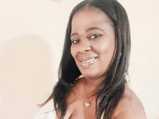 LinsayHott with dark, straight hair, smiling, showing white teeth, wearing a heart necklace, and a white top, has a cute, sexy face with medium-sized, perky tits.
