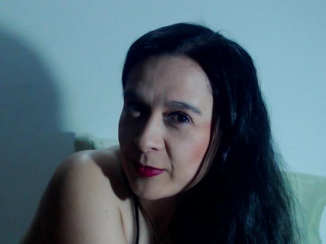 AileenRamirezW has black hair, red lipstick, and a subtle smile. She's topless with visible shoulders, looking slightly to the side with soft lighting.