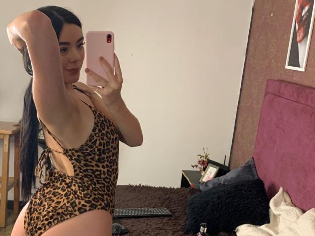 Samantha Chasse, con lunghi capelli neri, indossa un costume intero a stampa leopardo, che mostra l'ascella e il seno, e sta scattando un selfie allo specchio con un telefono rosa in una camera da letto..