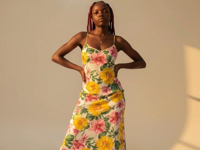 EbonyDivaa-hot in a floral dress, yellow and pink flowers, white background, standing with hands on hips, braided red hair, slim build, small tits, dark skin, confident pose.