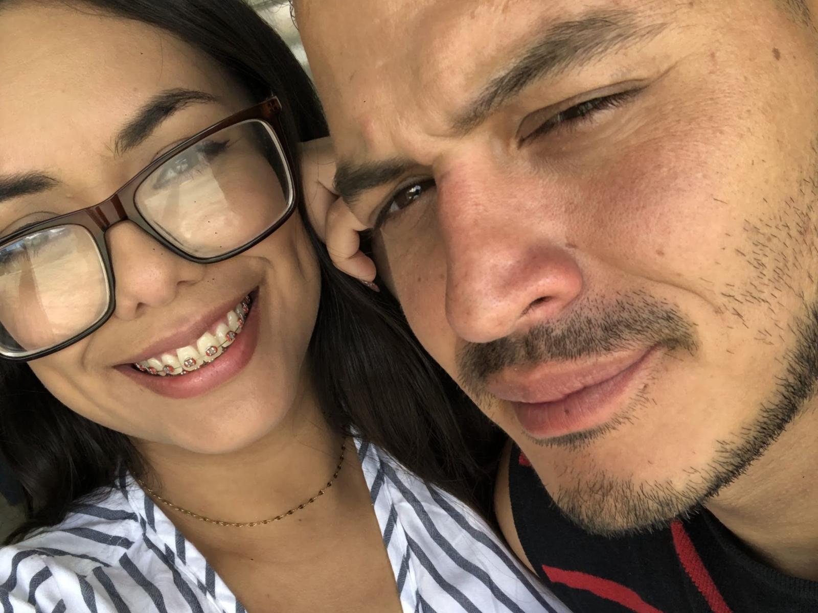 MikeAndLunaa met een bril, lachend, met zichtbare metalen beugels, naast een kale Mike met een snor en een lichte frons, die een zwart en rood shirt draagt..